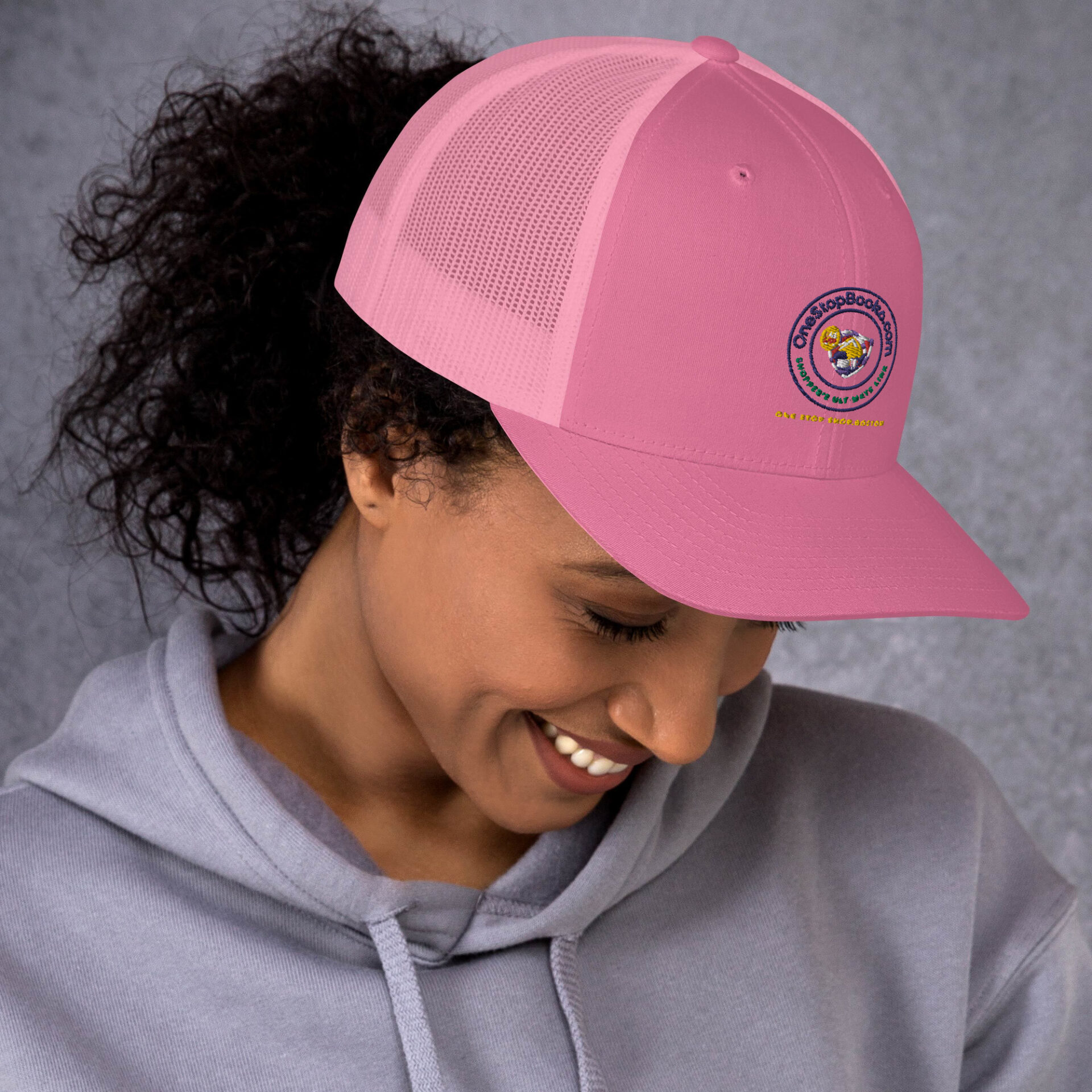 Woman smiling, wearing pink hat with logo.