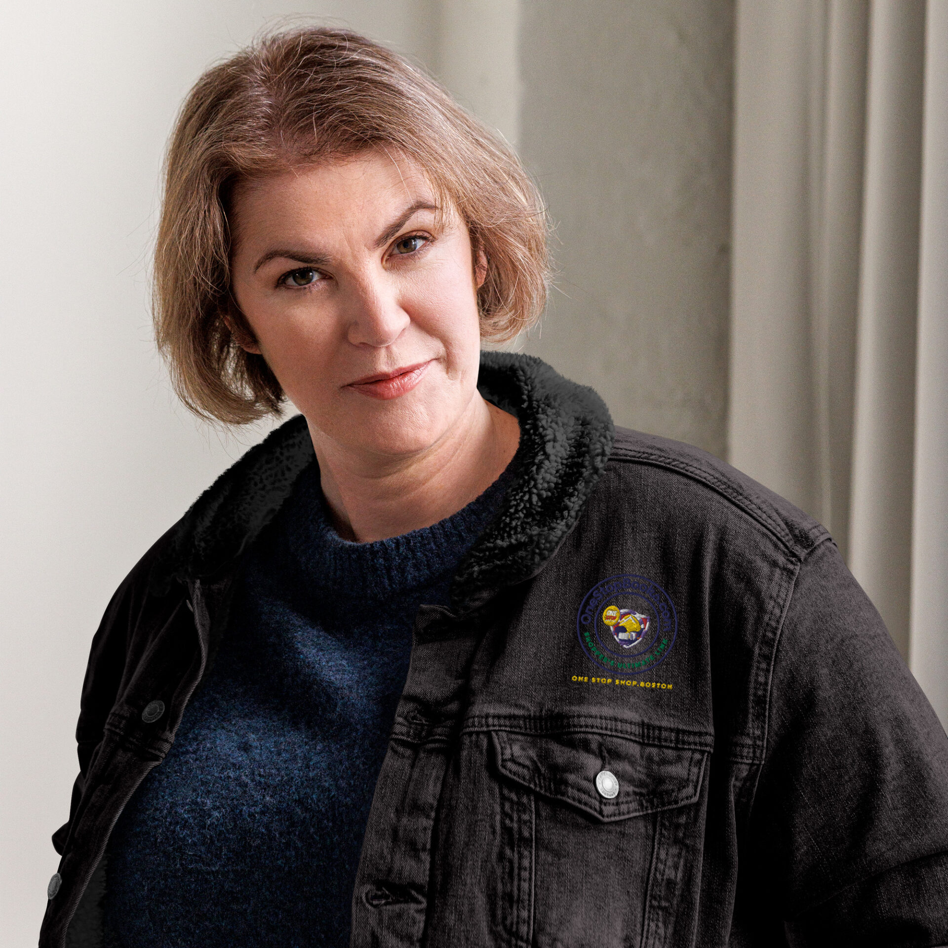 Woman in black denim jacket with logo.